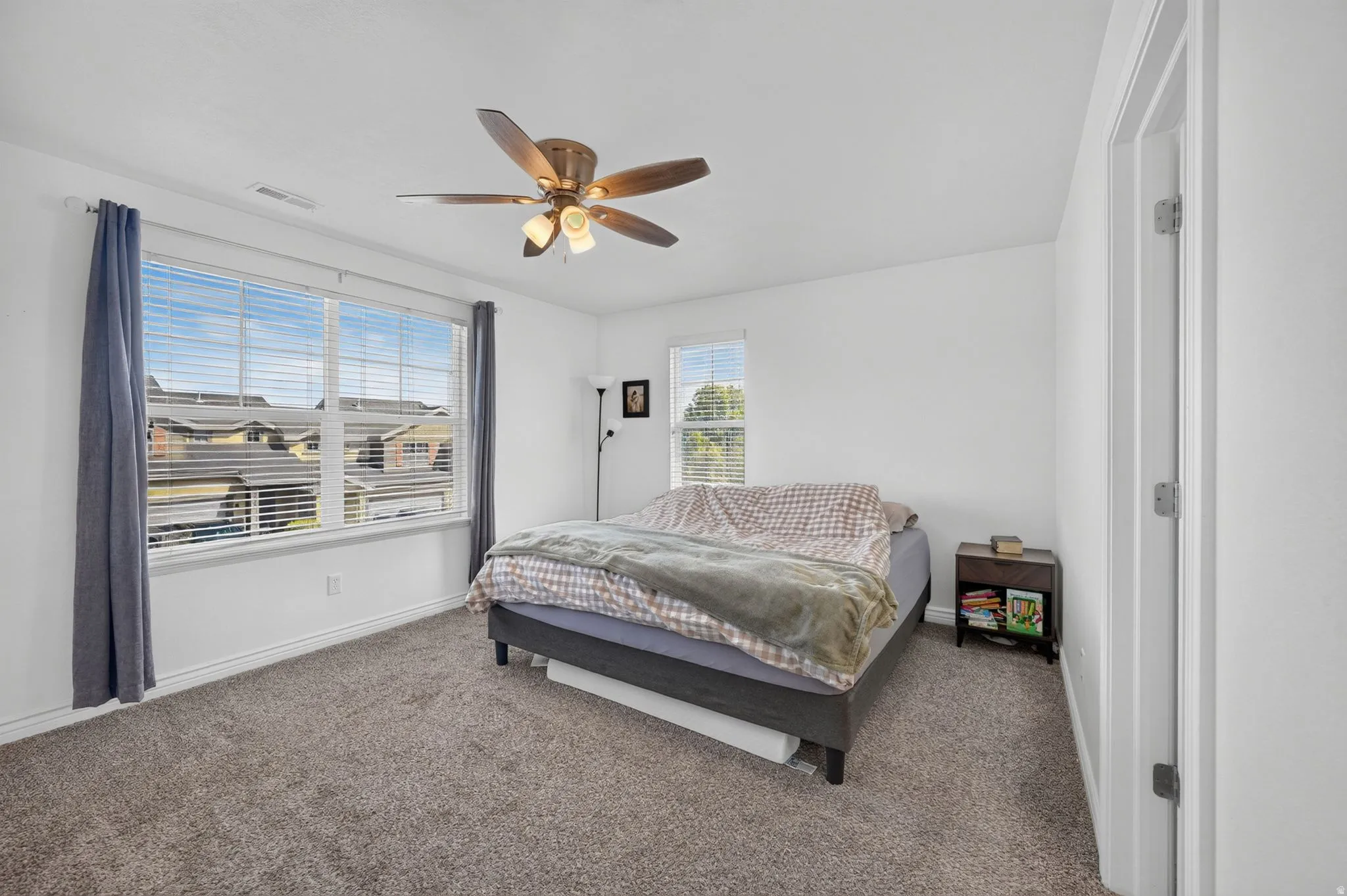 Bright room featuring a large window with blinds, a ceiling fan, and carpeted flooring