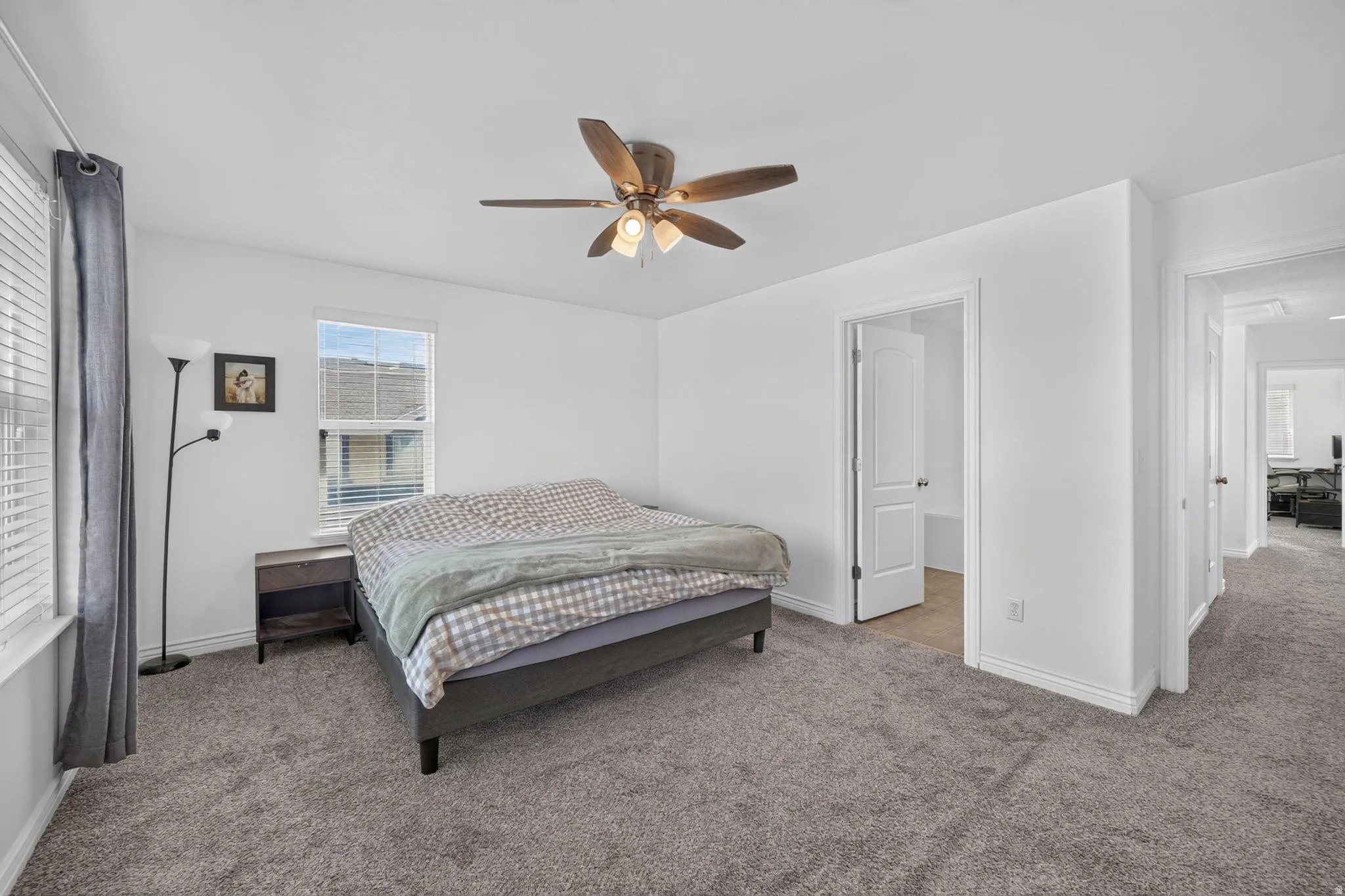 Spacious room featuring neutral carpeting, white walls, a ceiling fan with integrated lighting, and a window with blinds