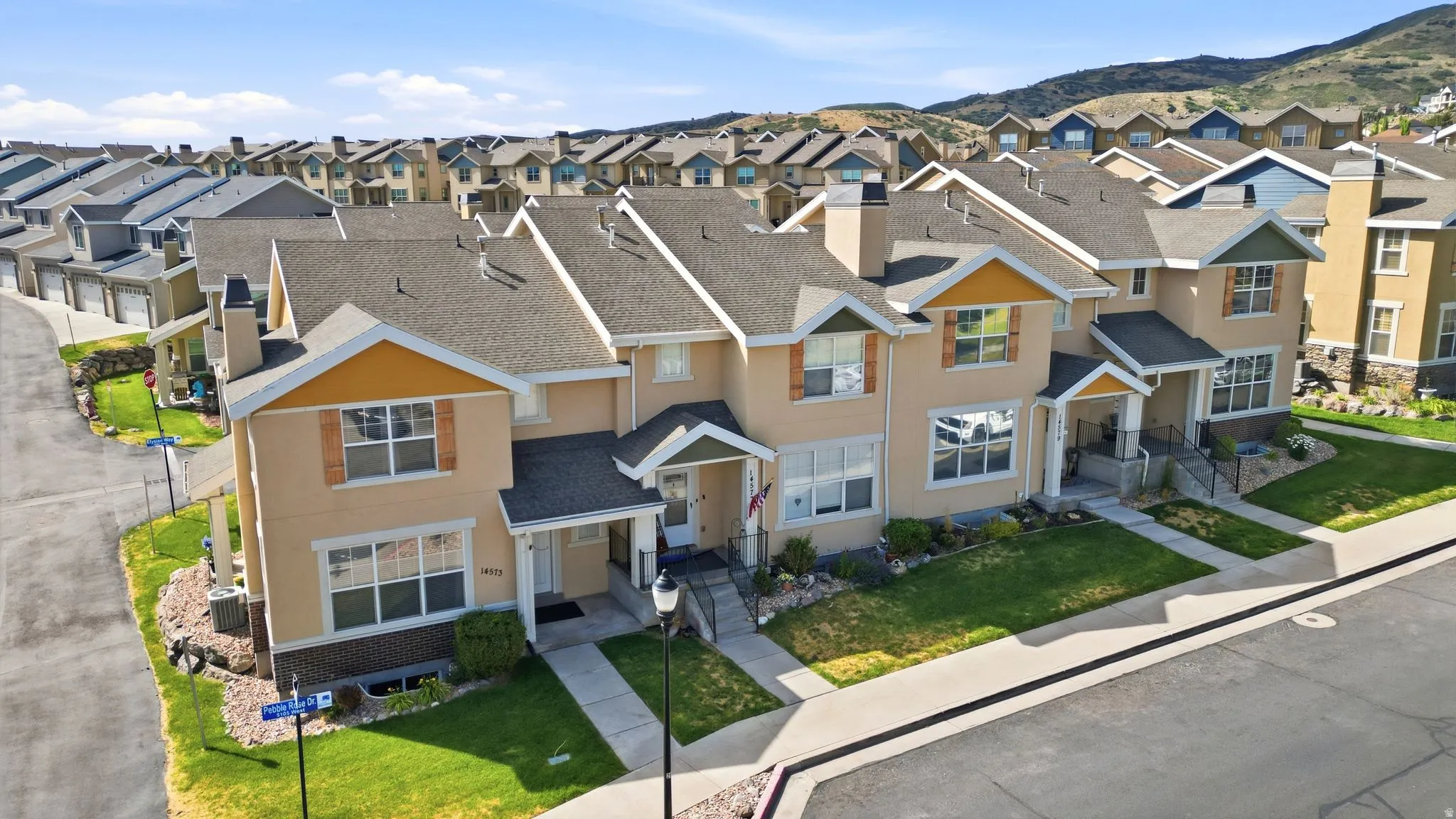 Townhome exterior featuring tan stucco siding, brown shingle roofing, and decorative shutters