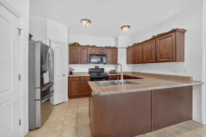 Kitchen featuring wood cabinetry, light-toned countertops, a stainless steel double-basin sink with a gooseneck faucet, and tile flooring
