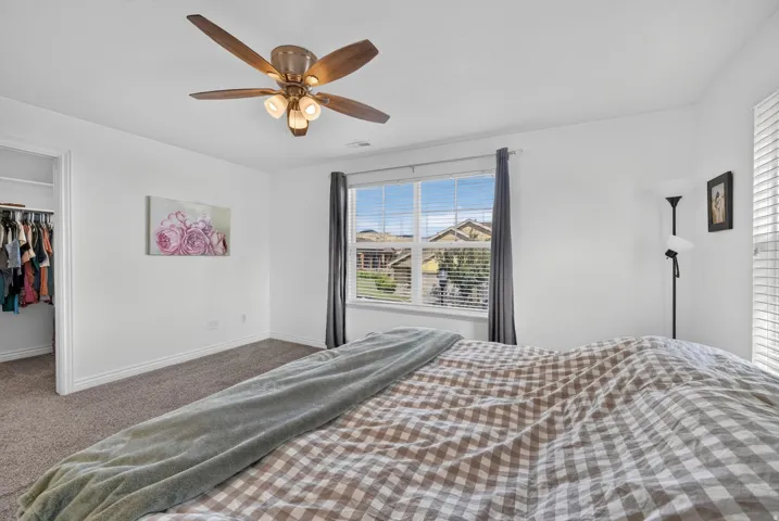Carpeted bedroom featuring a large window with blinds, a ceiling fan with integrated lighting, and an open closet
