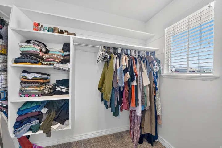 Walk-in closet featuring built-in white shelving, integrated hanging rods, and a window with blinds
