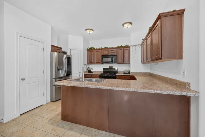 Kitchen featuring wood-finish cabinetry, speckled countertops, stainless steel refrigerator, black range, and dual-basin sink