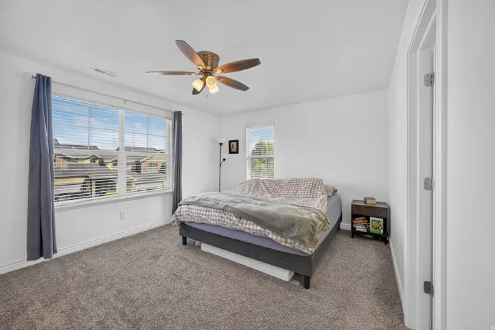 Bright room featuring a large window with blinds, a ceiling fan, and carpeted flooring
