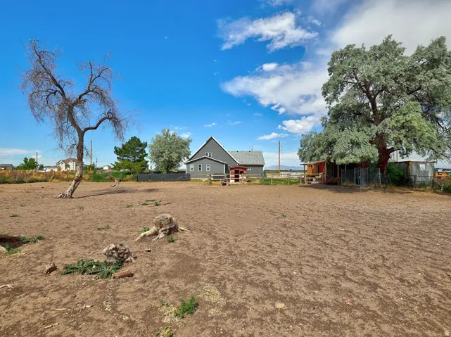 Expansive open lot with a detached gray house featuring white trim
