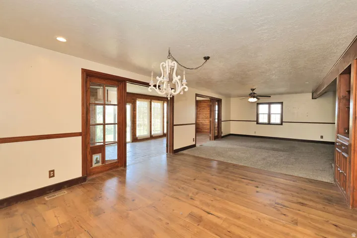 Open-concept room featuring wood-finish flooring, a decorative chandelier, and a wood-framed glass door opening to an additional room with multi-pane windows