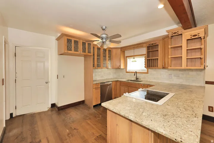Kitchen featuring wood-finish flooring, light-toned cabinetry, light-colored tile backsplash, a built-in cooktop, and a stainless steel dishwasher