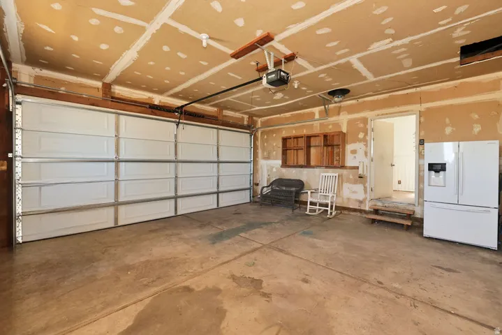 Spacious garage featuring a large paneled door, exposed ceiling joists, wood-finish wall shelving, and concrete flooring