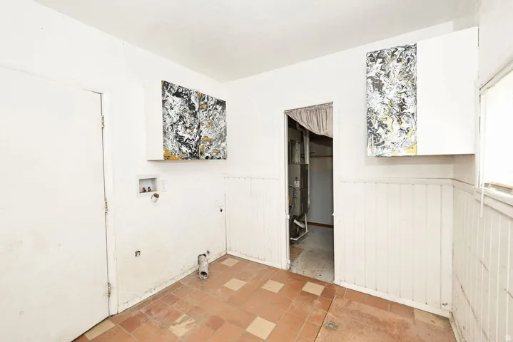 Laundry area featuring a terracotta-toned tiled floor, white beadboard paneling, and two wall-mounted storage cabinets