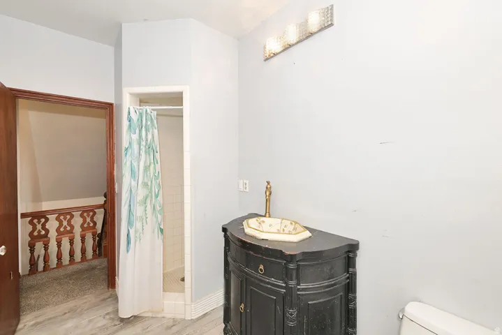 Bathroom featuring a corner shower stall with white tile surround, a dark wood vanity with an ornamental basin and brass-tone faucet, and a three-light vanity fixture