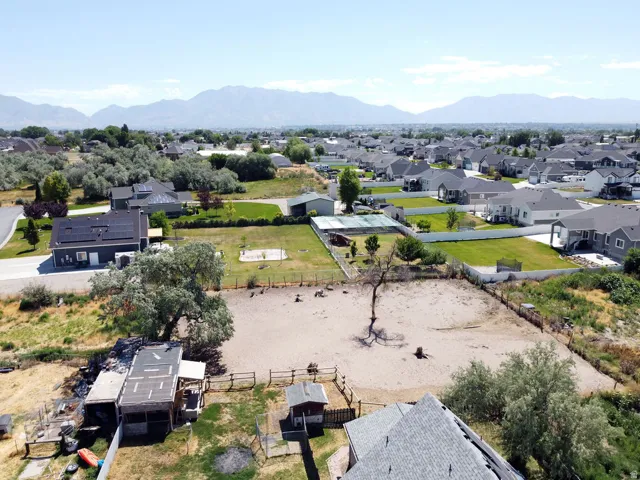 Expansive lot with fencing, outbuildings, and mature trees, set within a residential neighborhood with distant mountain ranges