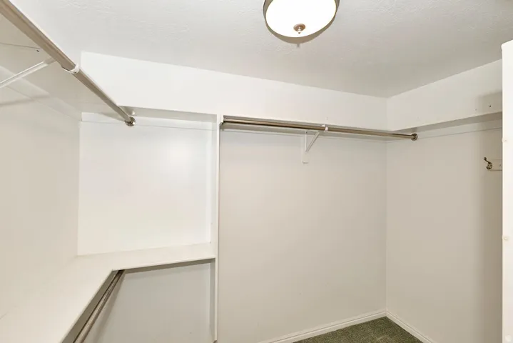Spacious closet featuring white painted walls, a flush-mount ceiling light fixture, and multiple chrome hanging rods