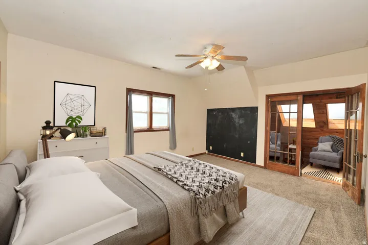 Carpeted room featuring a ceiling fan, a chalkboard wall, and an adjacent wood-paneled sunroom with skylights and glass-paned French doors