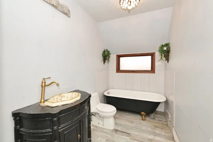Bathroom featuring a black clawfoot tub, wood-finish flooring, a wood-framed window, and wainscoting
