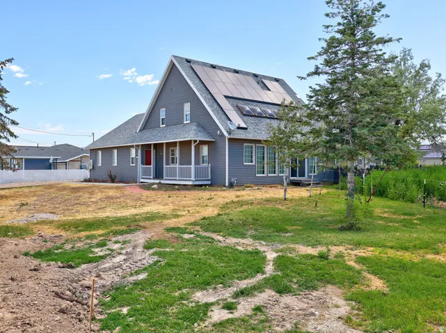 Gray siding residence featuring a red entry door, covered front porch, multiple solar panel arrays, and a white picket fence bordering the property