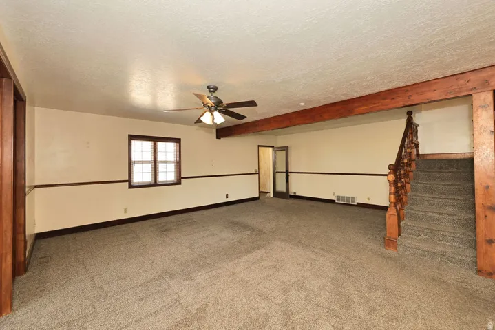 Spacious room featuring neutral carpeting, a ceiling fan with integrated lighting, and a wood-trimmed window