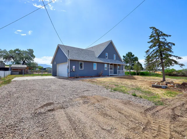 Gray siding exterior featuring a covered front porch with white railings, a two-car garage, and a gravel driveway