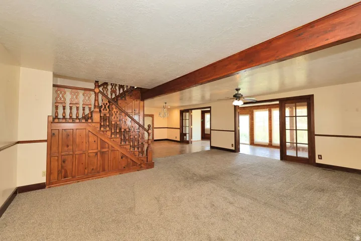 Spacious interior featuring a prominent wood staircase, exposed ceiling beam, and light-toned carpet flooring