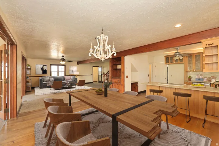 Open-concept living space featuring wood-finish flooring, exposed ceiling beams, a large kitchen island with bar seating, custom wood cabinetry, and a decorative chandelier
