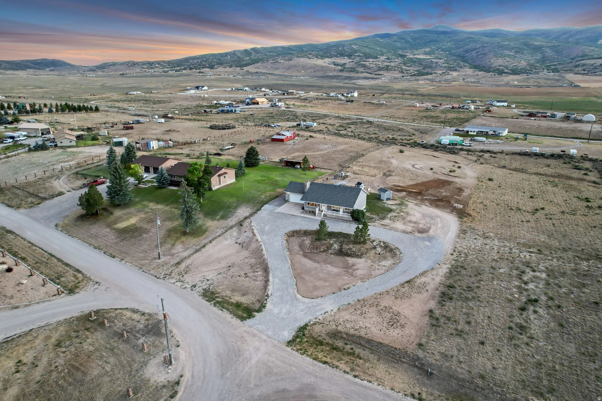 Expansive lot featuring a gravel driveway, mature evergreen trees, and a distant mountainous backdrop