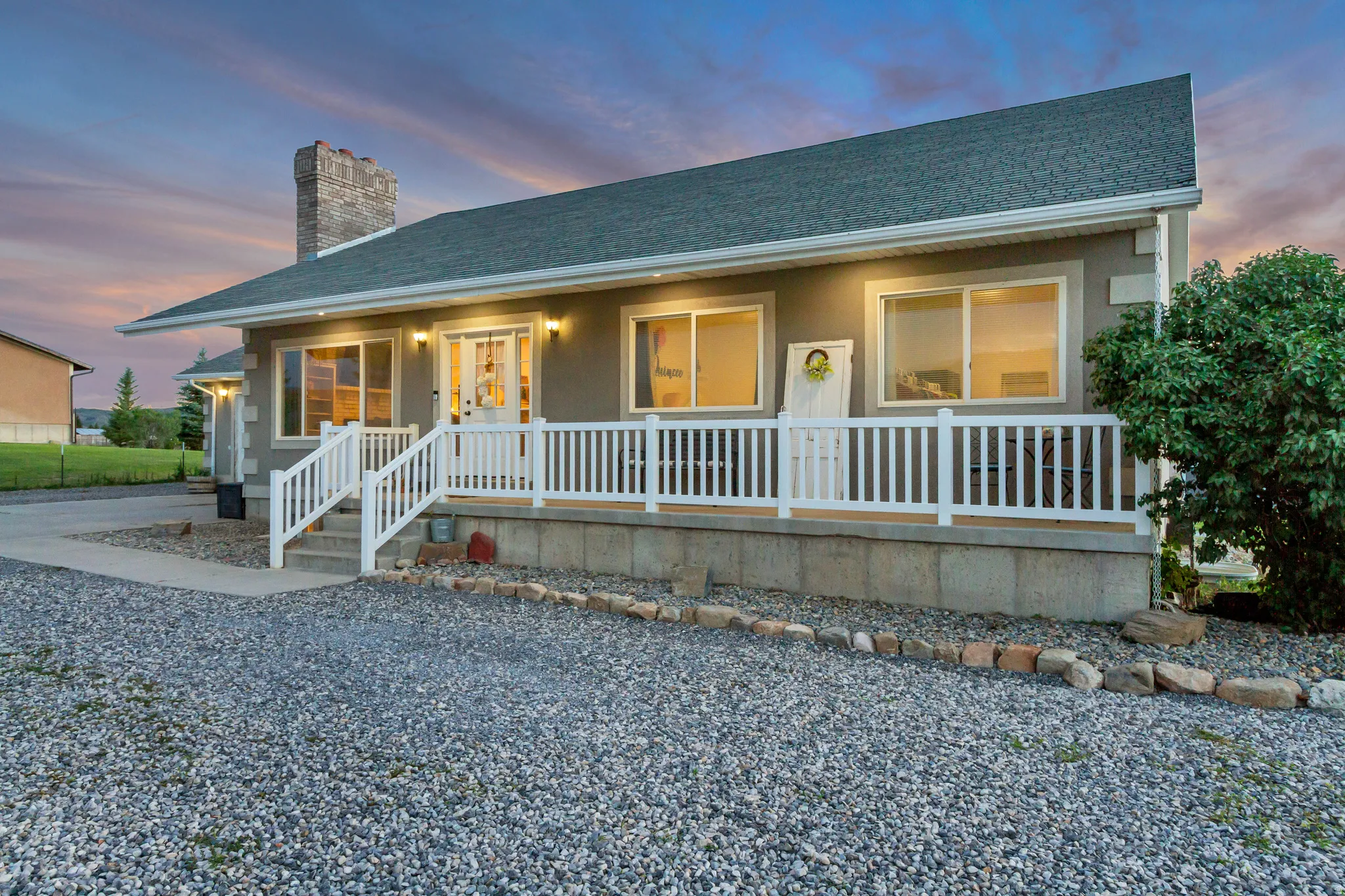 Stucco exterior featuring a dark green shingled roof and a prominent stone chimney