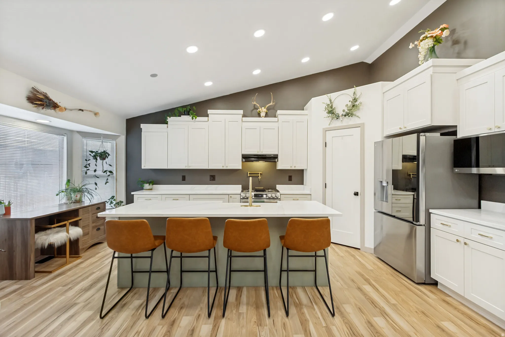 Bright kitchen featuring an expansive center island with seating, white shaker cabinetry, stainless steel appliances, and wood-finish flooring