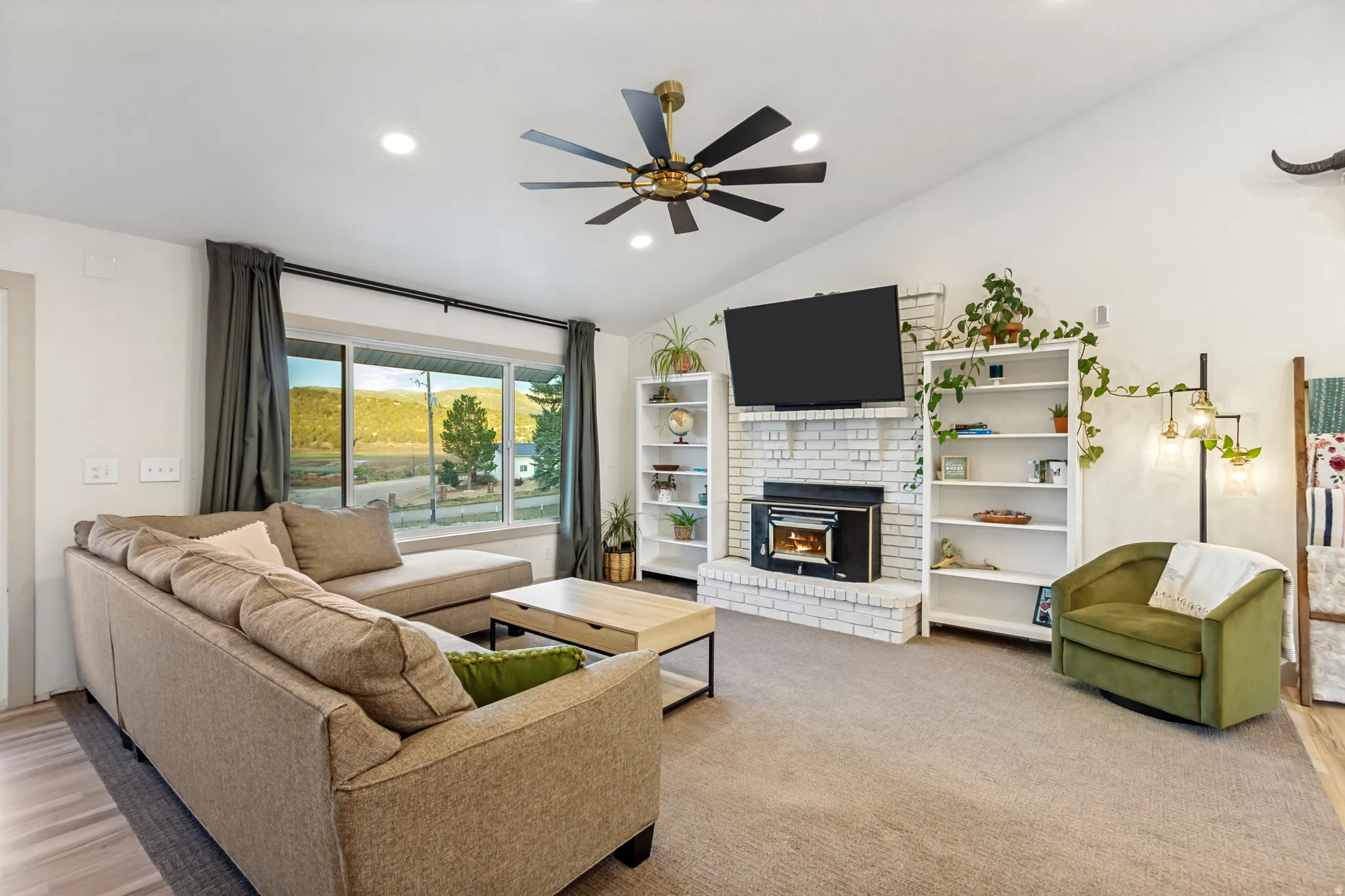 Living area featuring a vaulted ceiling with a ceiling fan, a white brick fireplace with an insert, recessed lighting, and a large window with a deep sill
