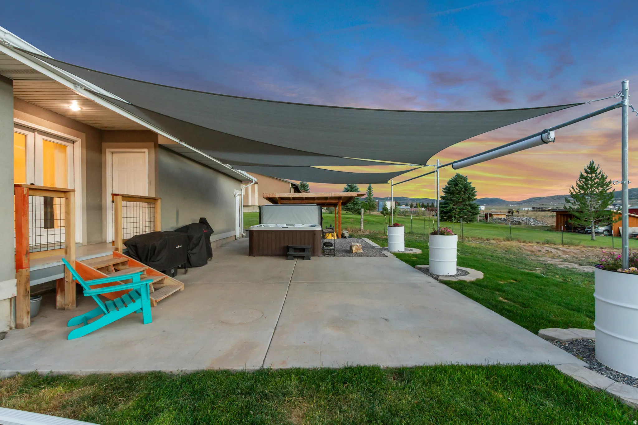 Expansive concrete patio featuring a hot tub, a partially covered pergola, and a large shade sail structure