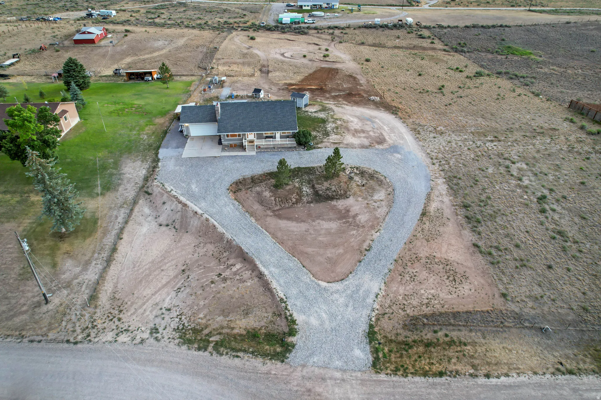Expansive property featuring a gravel circular driveway, a single-story residence with an attached carport, and a substantial undeveloped land area