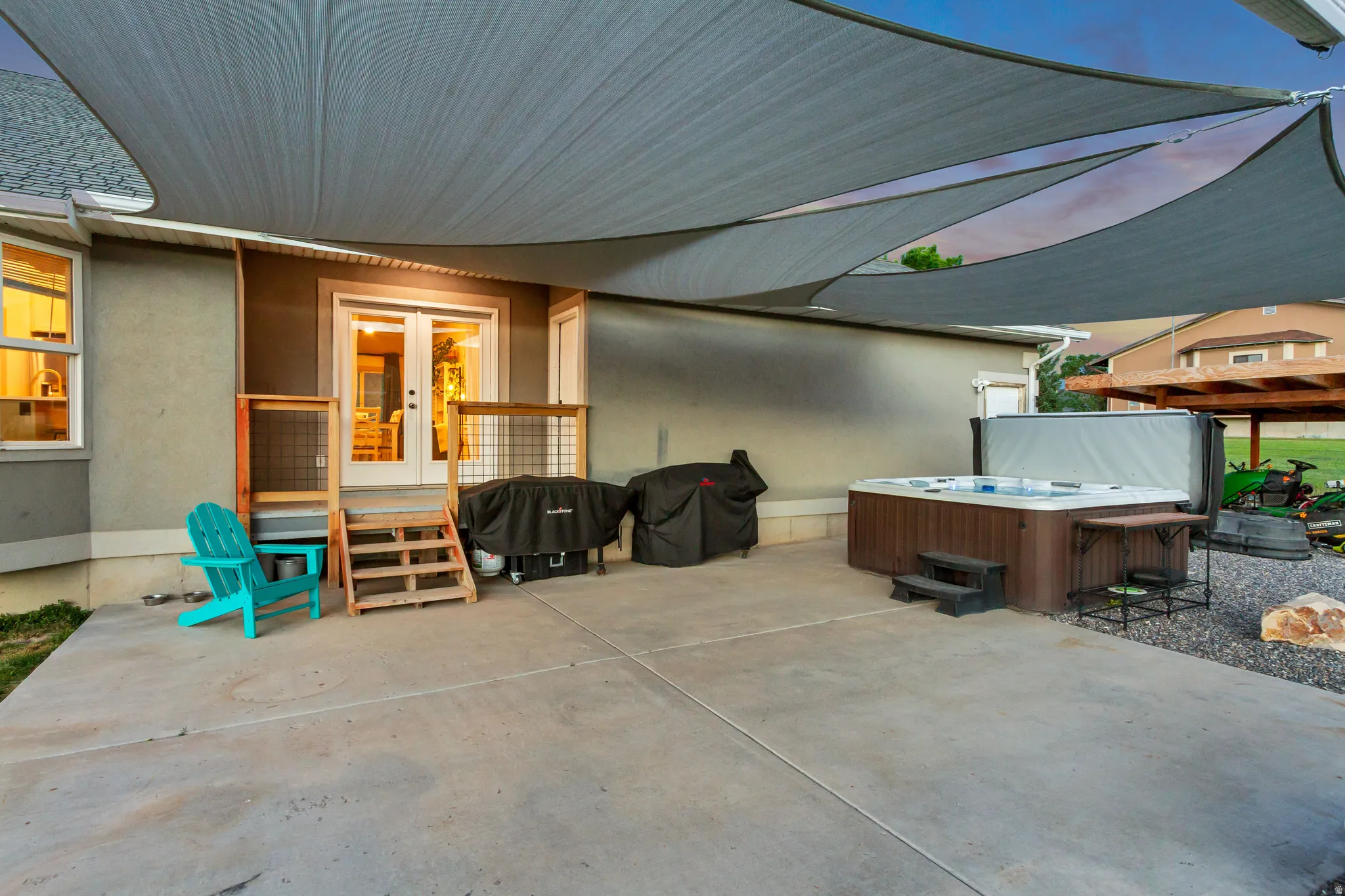 Expansive concrete patio featuring multiple shade sails, a built-in hot tub, and direct access to interior spaces via double French doors