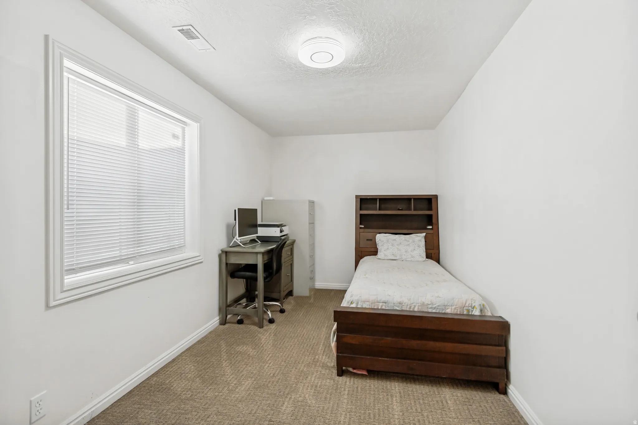 Carpeted interior room with white walls and a single window featuring horizontal blinds