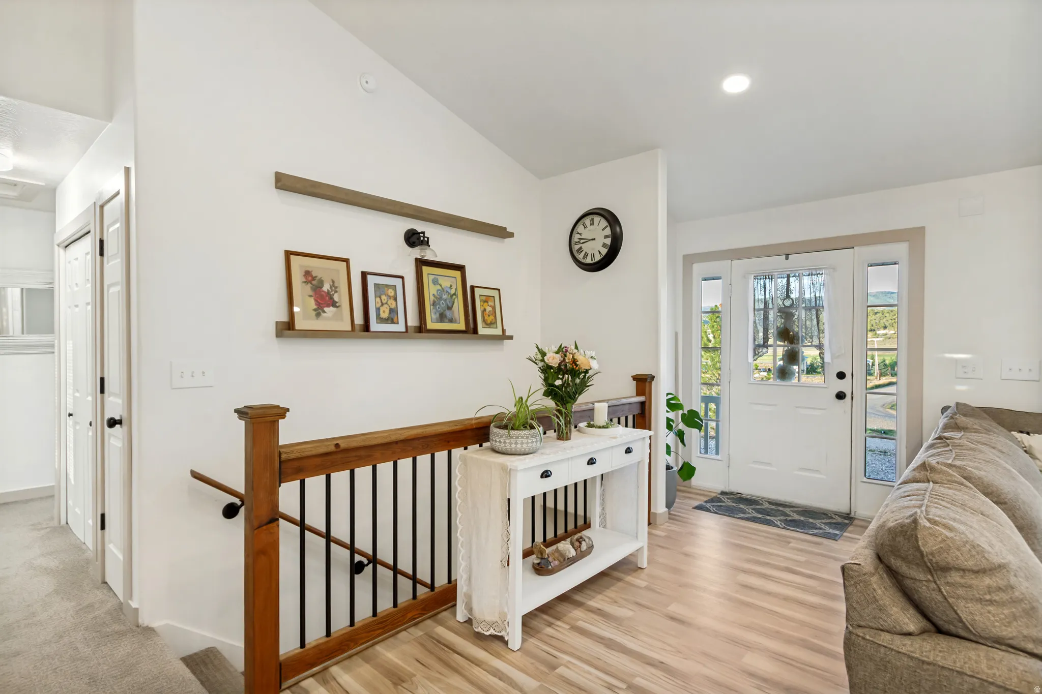 Entryway featuring a paneled front door with sidelight windows, vaulted ceilings, wood-finish flooring, and a craftsman-style wood and iron staircase railing