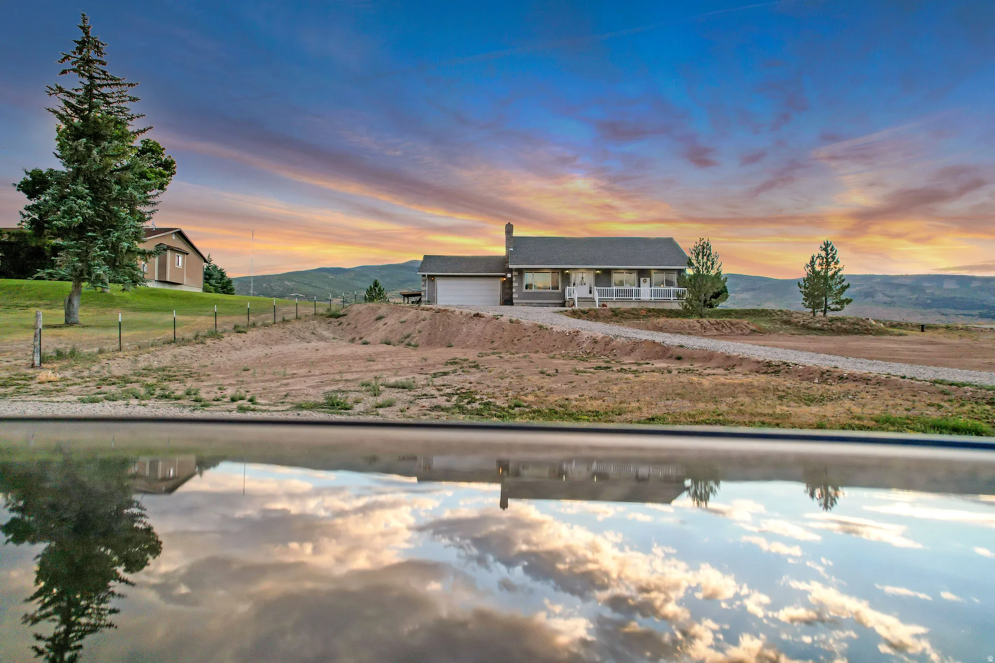 Ranch-style residence featuring a covered front porch with white railing, an attached two-car garage, and a gravel driveway