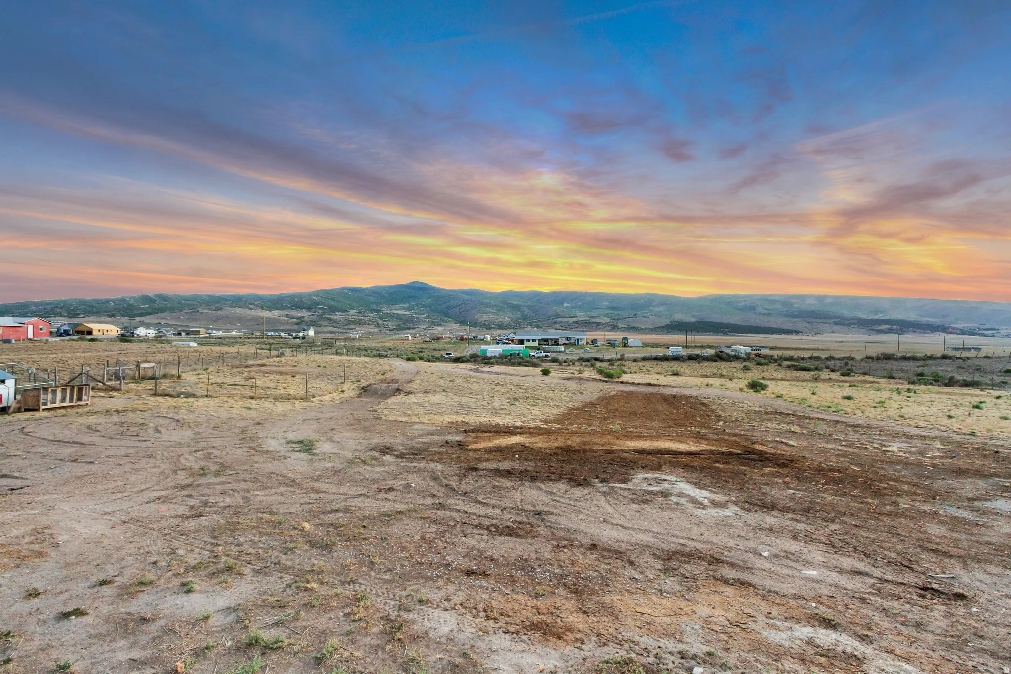 Expansive undeveloped land featuring a broad, flat terrain, distant mountains, and scattered structures on the horizon