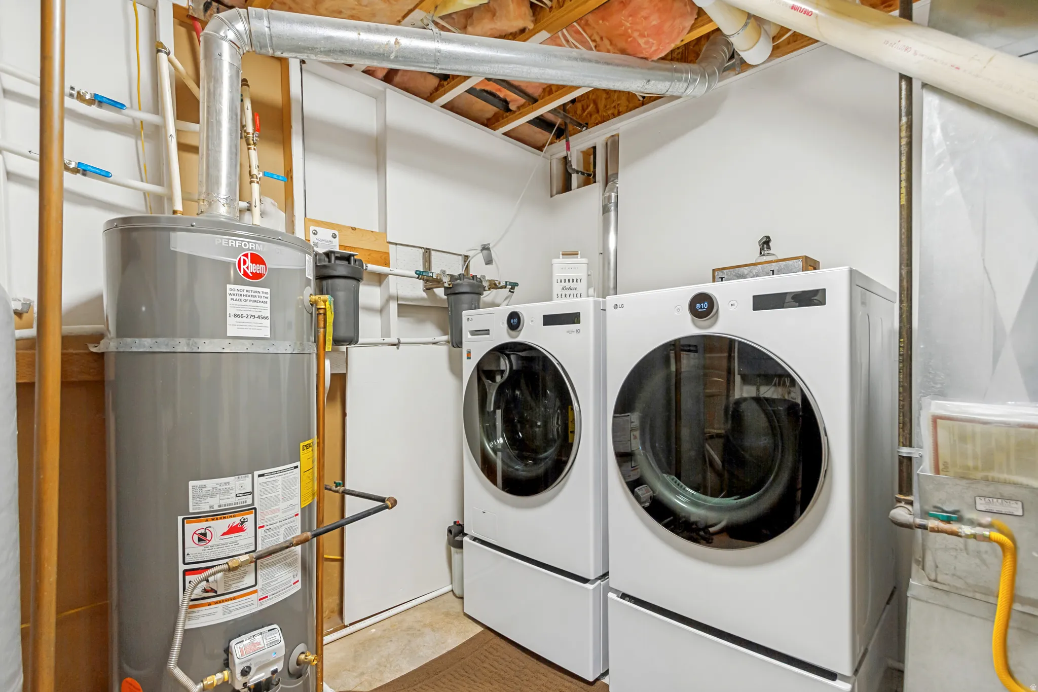 Laundry area featuring front-loading washer and dryer units with pedestals, a water heater, and visible utility connections