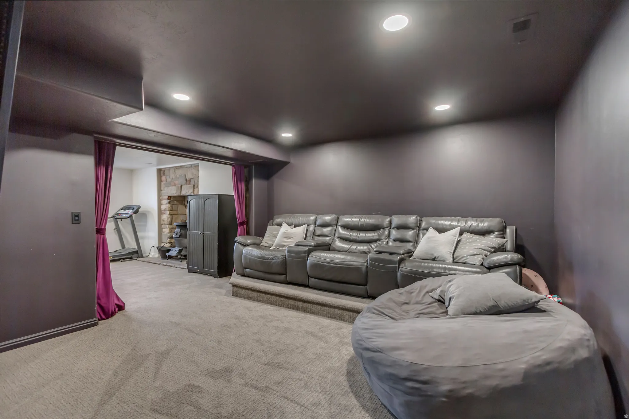 Spacious recreation room featuring recessed lighting, a neutral carpet, and direct access to an additional functional area with a stone wall accent