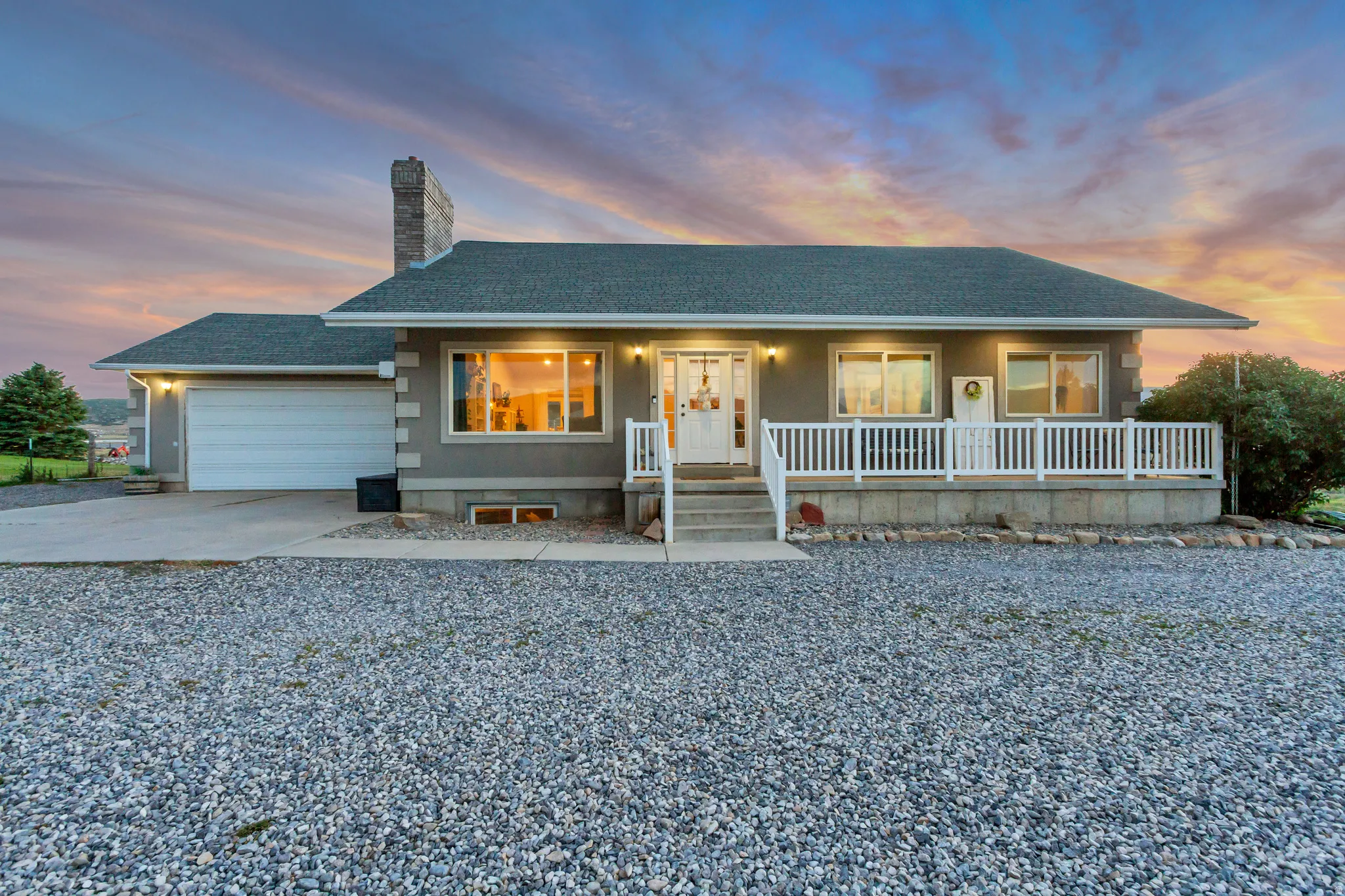 Ranch-style residence featuring a gray exterior, white porch railing, and an attached garage with a concrete driveway