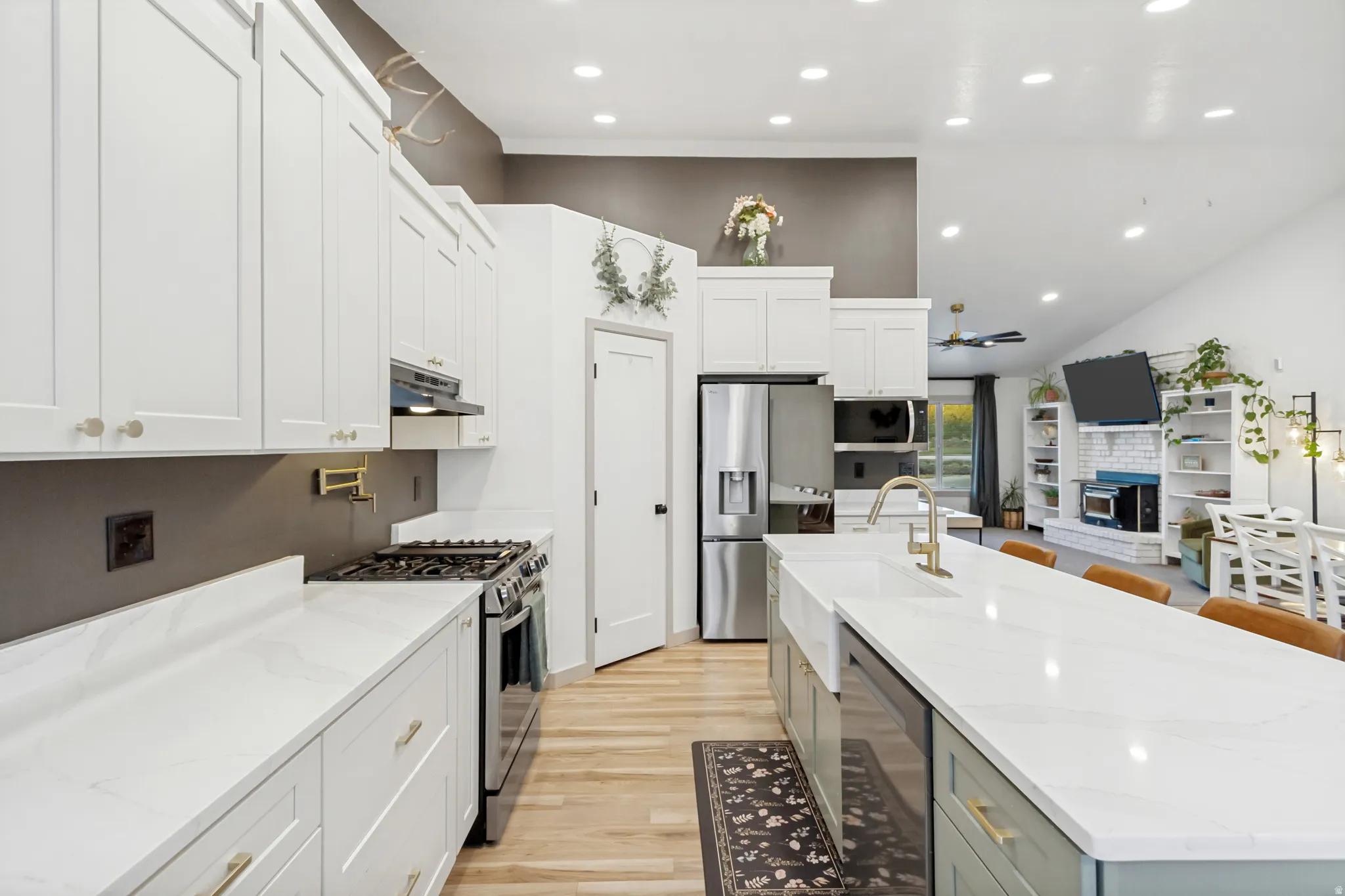 Bright kitchen featuring white shaker cabinetry, stainless steel appliances, a center island with an integrated sink, white countertops, and wood-finish flooring