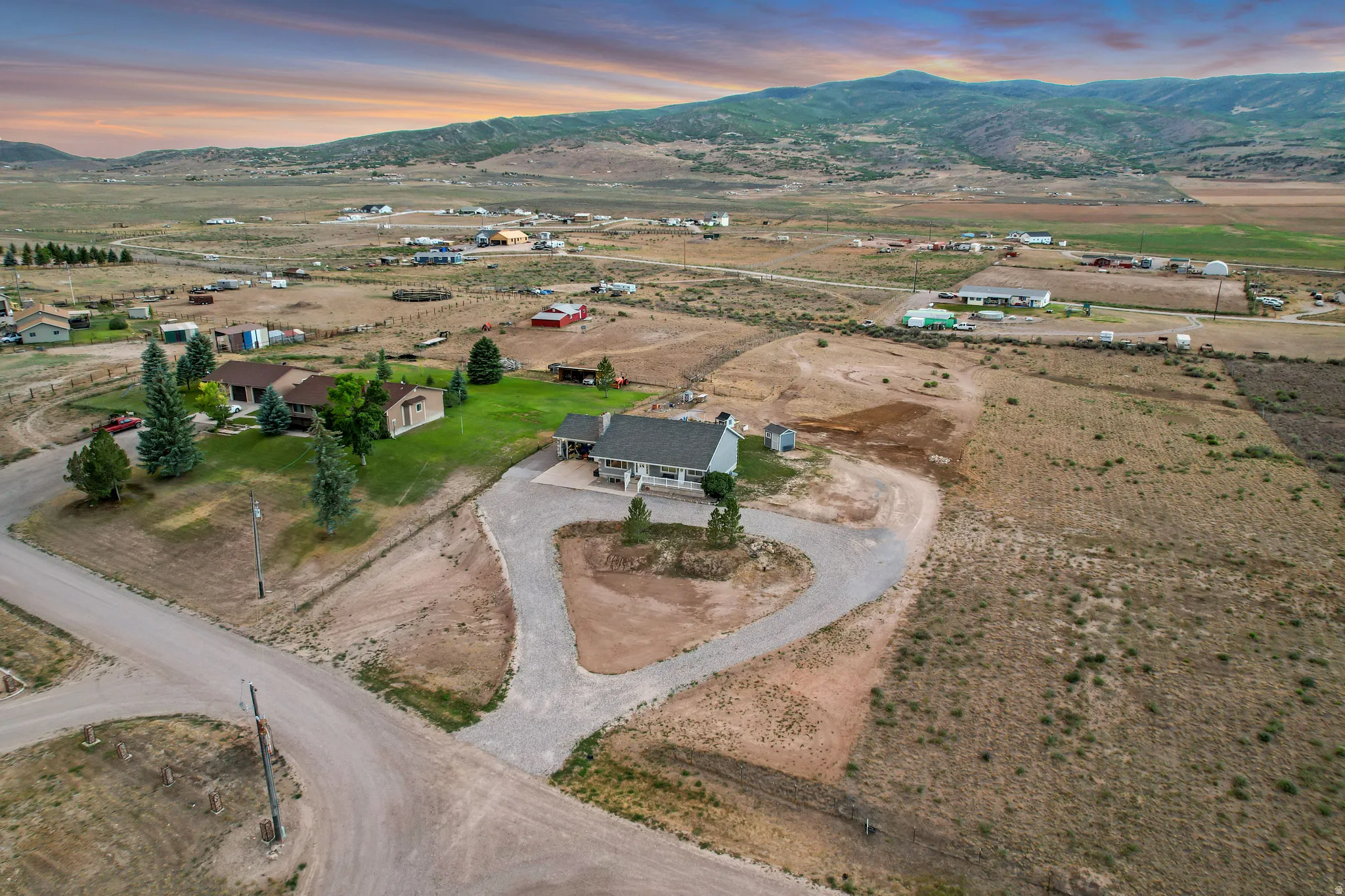 Expansive property featuring a gravel driveway, mature evergreen trees, and surrounding open terrain