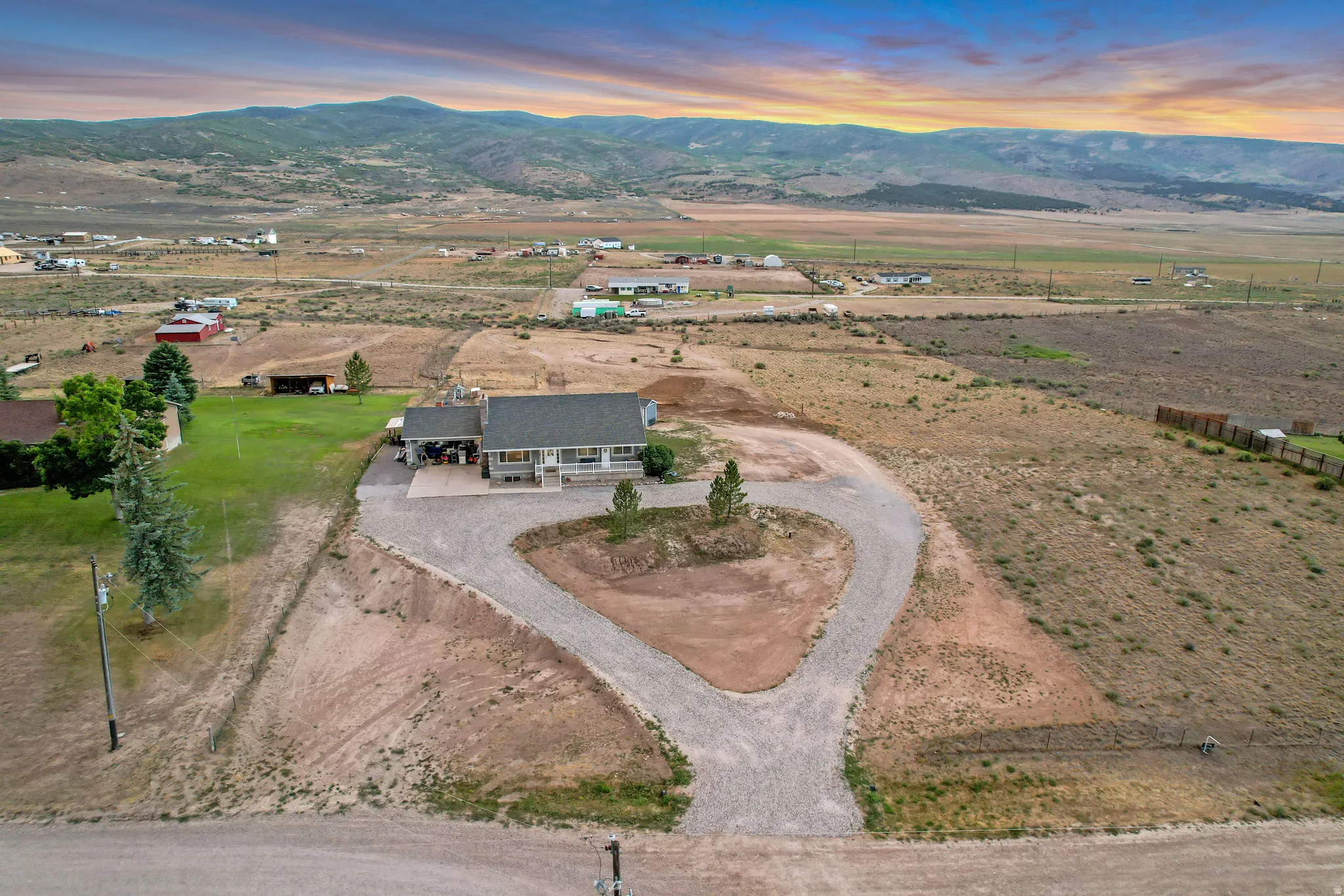 Expansive property featuring a single-story residence with a covered front porch, a gravel U-shaped driveway, and a large grassy area