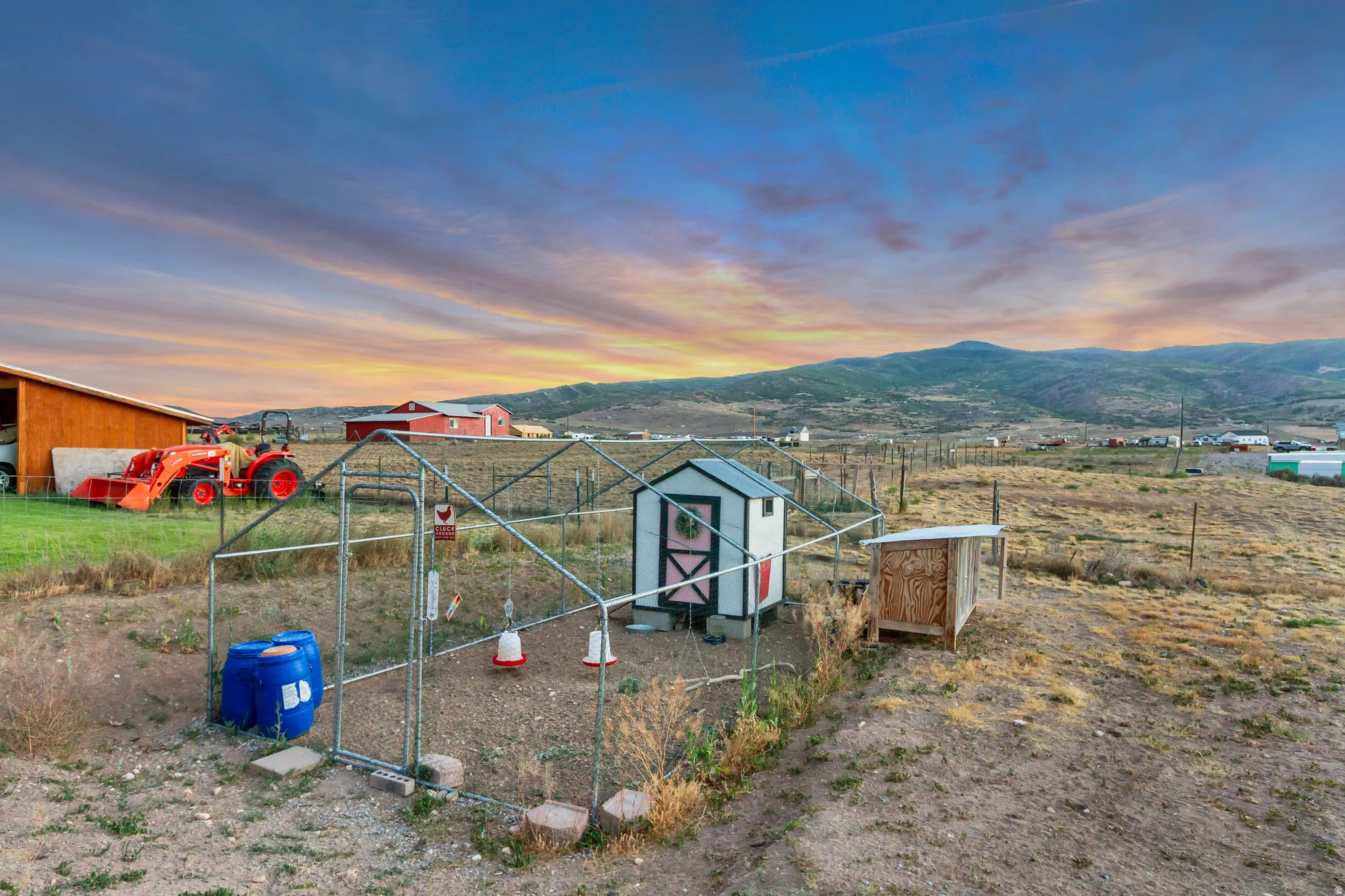 Fenced enclosure featuring a white and pink chicken coop with a covered run and an additional wooden structure