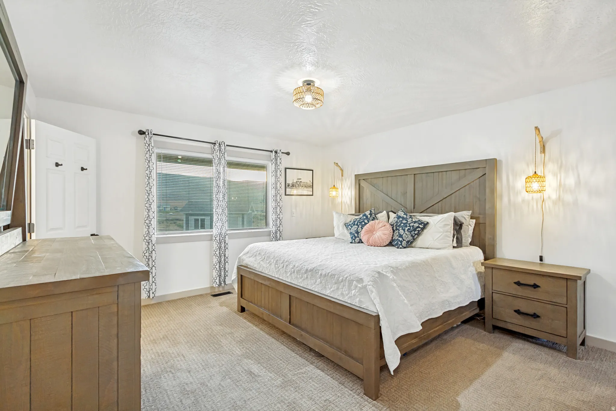 Bright bedroom with light-colored carpeting, featuring a window with blinds and curtains