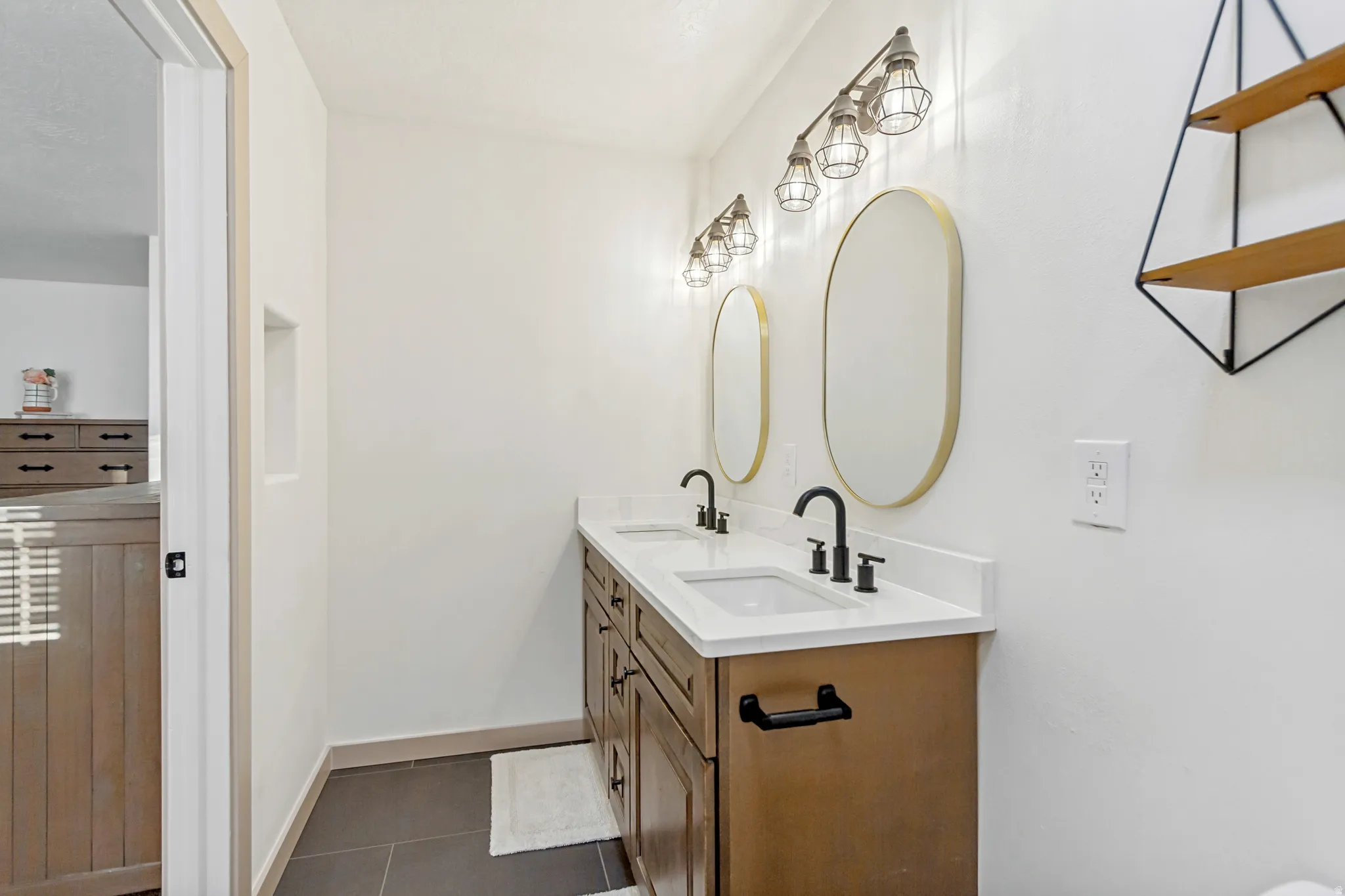 Double vanity featuring a light-toned wood-finish cabinet, white solid surface countertop, and dual oval mirrors with brass-finish frames