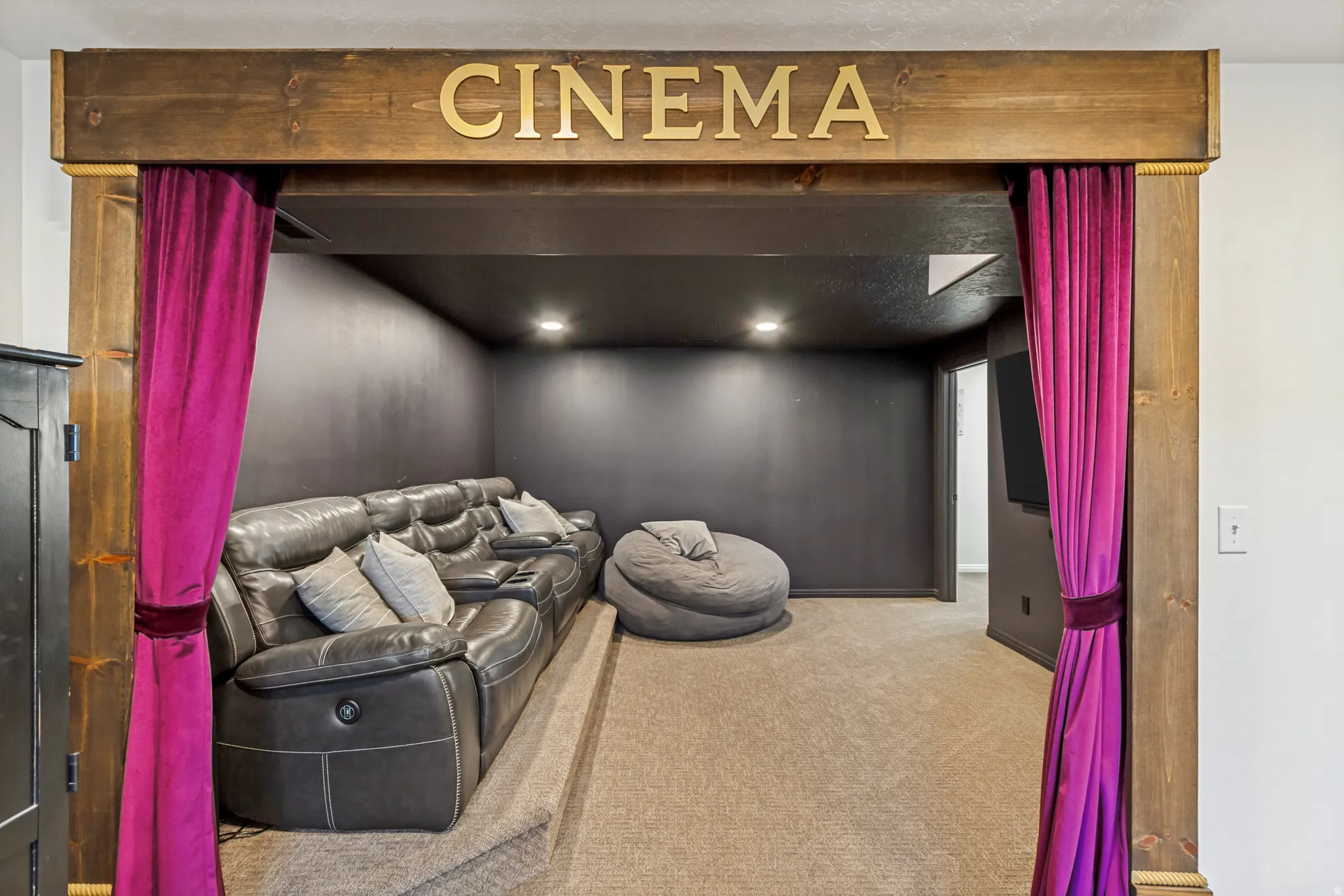 Dedicated cinema space featuring a wood-finish archway with "CINEMA" lettering, recessed lighting, and dark wall finishes