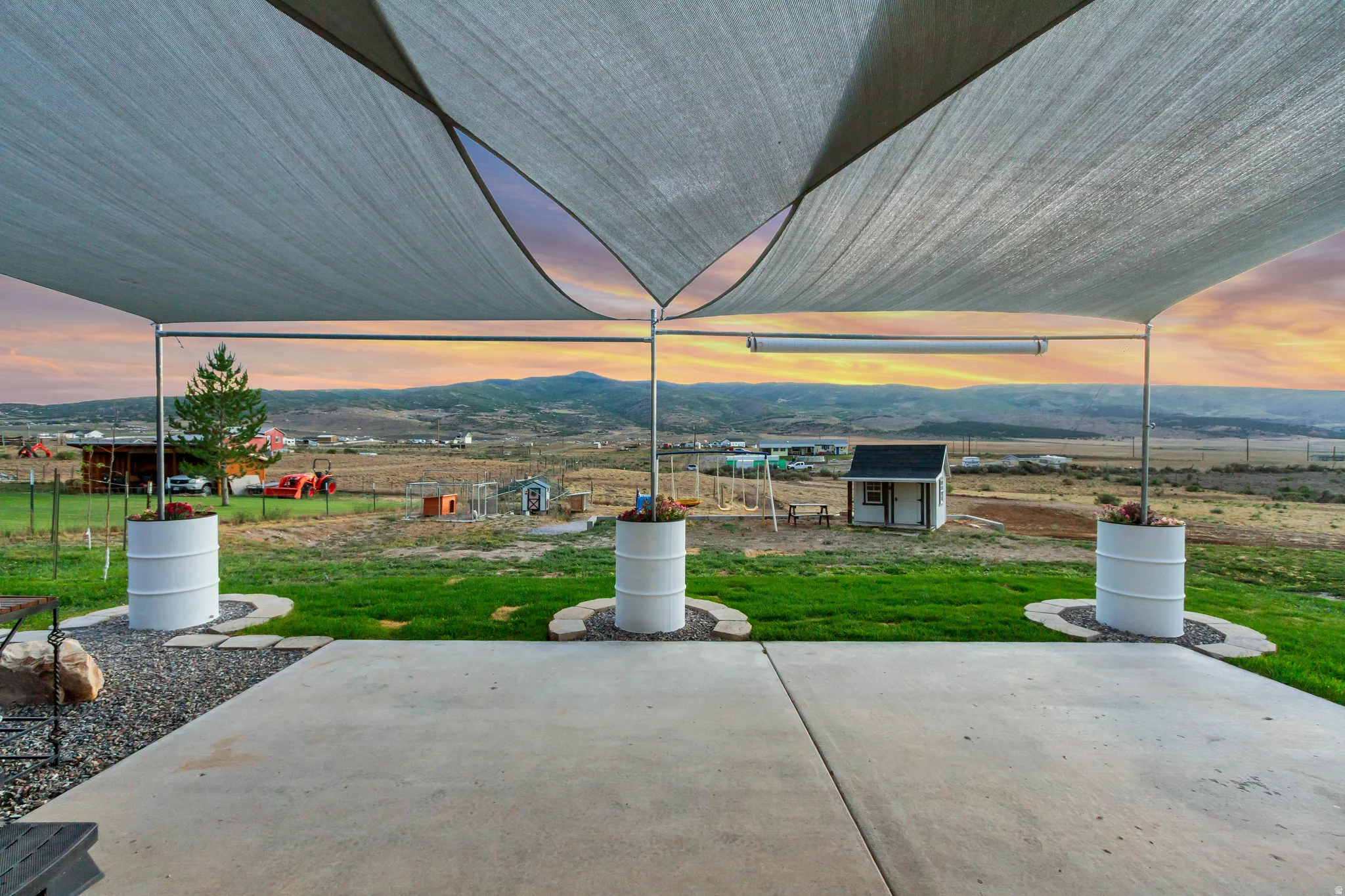 Expansive outdoor patio featuring a shade sail canopy, concrete flooring, and decorative planters