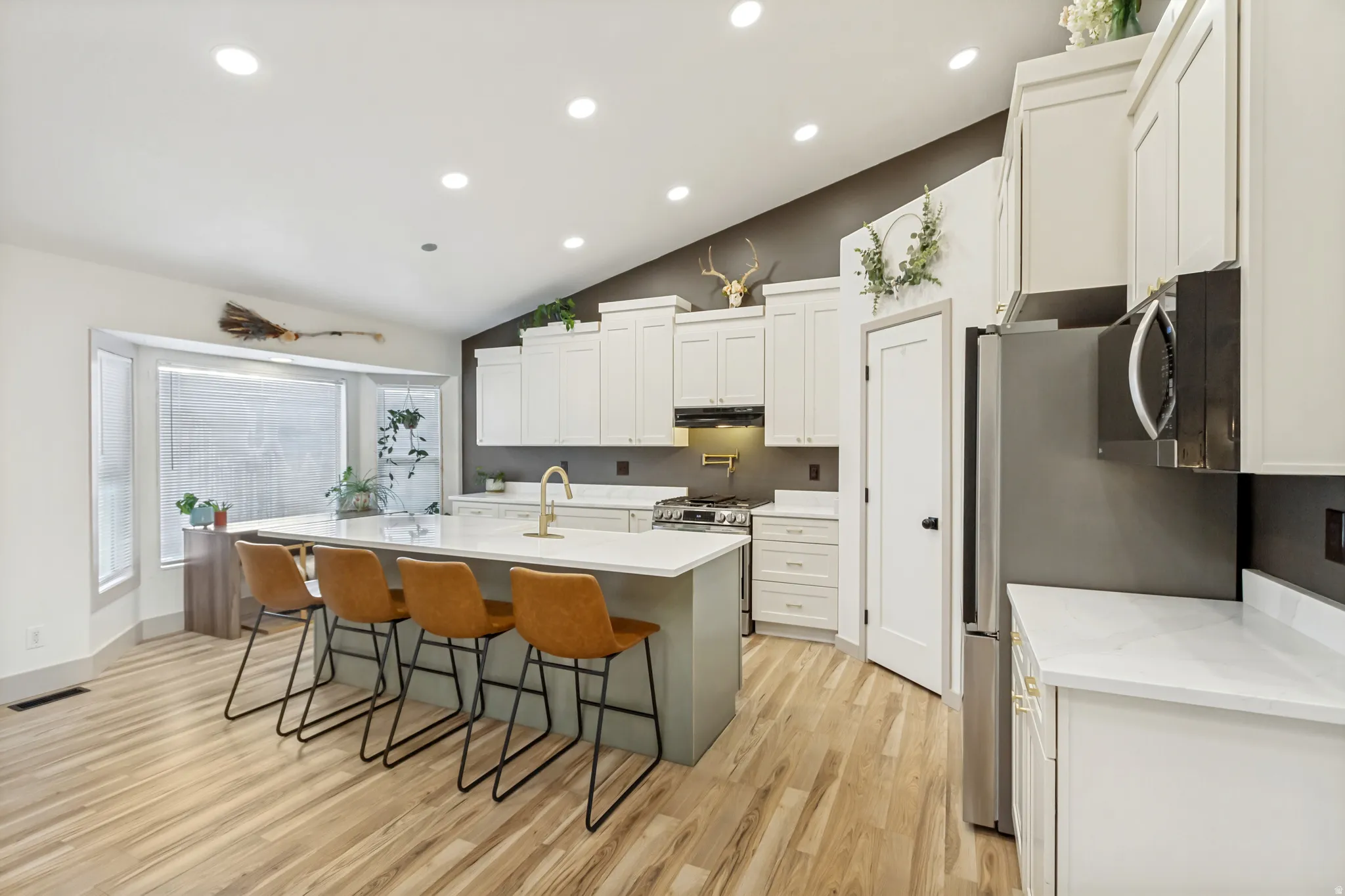 Open-concept kitchen featuring an oversized island with seating, recessed lighting, wood-finish flooring, white cabinetry, and stainless steel appliances