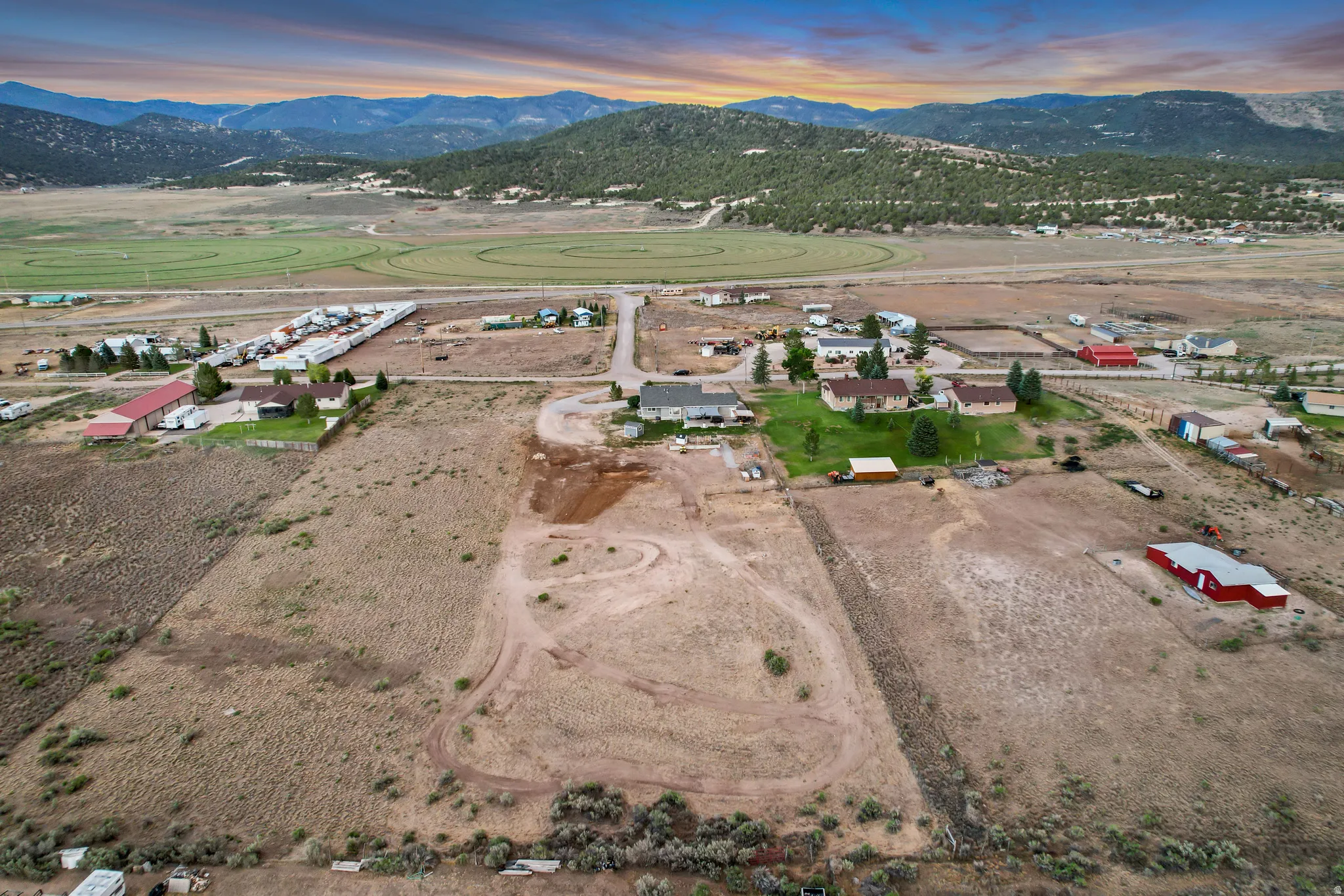 Expansive aerial property featuring undeveloped land, scattered structures, and distant mountains