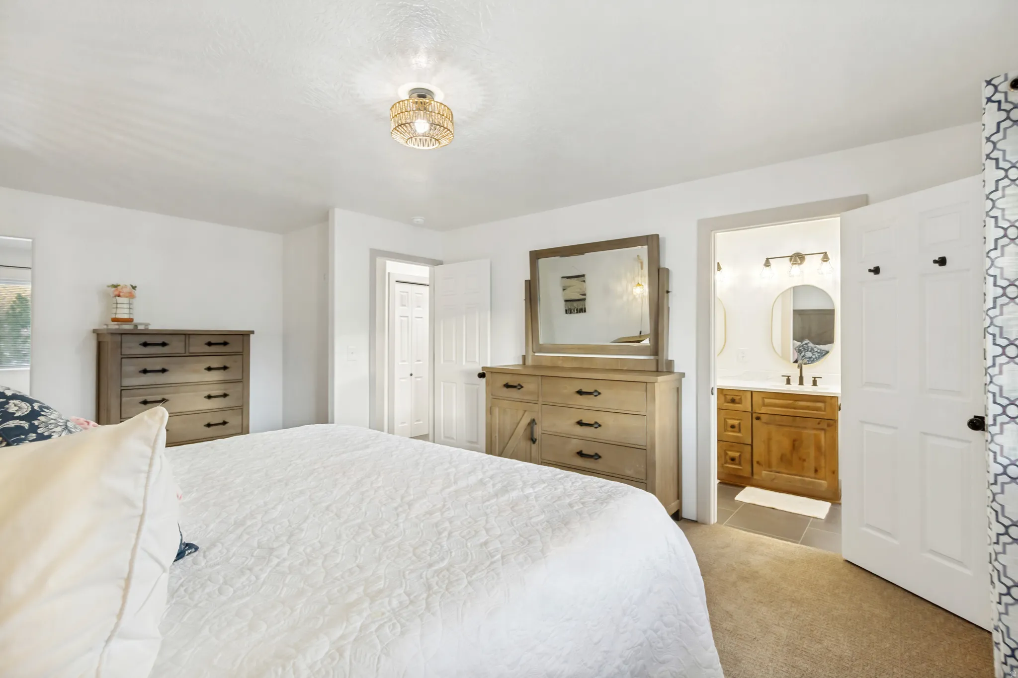 Carpeted bedroom area featuring a light-toned wood-finish dresser with a mirror, a modern ceiling light fixture, and a doorway opening to a bathroom