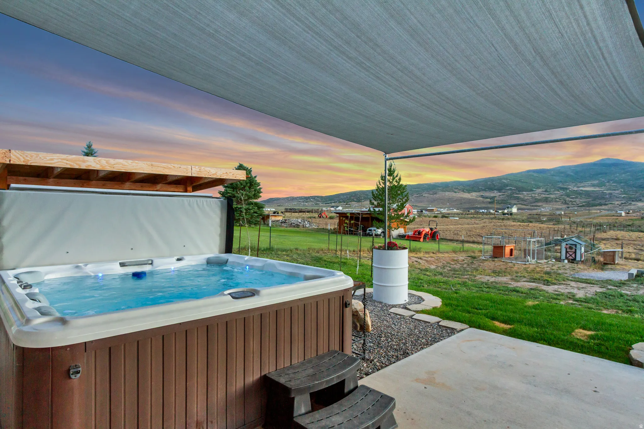 Outdoor spa with wood-look surround, integrated steps, and a retractable cover, situated on a concrete patio
