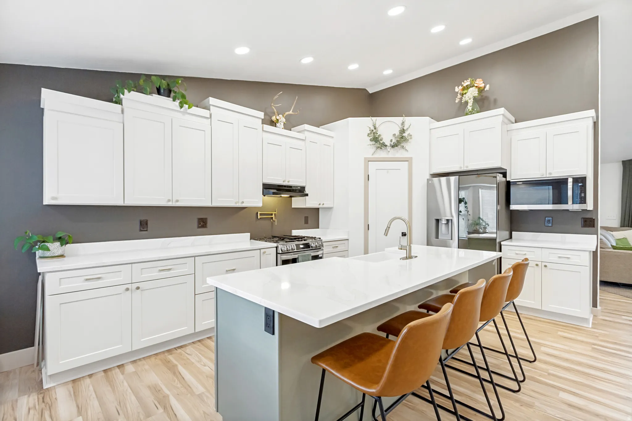 Spacious kitchen featuring an expansive central island with seating, white shaker-style cabinetry, stainless steel appliances, light wood-finish flooring, and recessed lighting